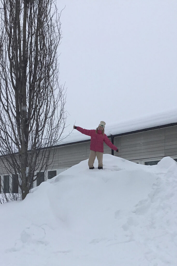 En elev i rosa jacka står högst upp på en stor snöhög.