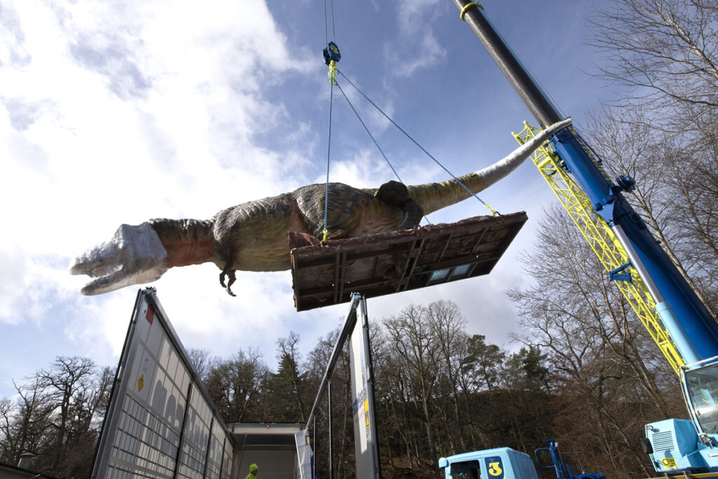 En stor dinosaurie som lyfts ur en lastbil med en lyftkran.