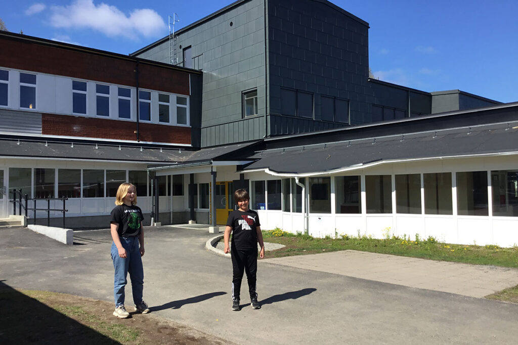 Två elever som står framför Pitholmsskolans nya tillbyggnad.